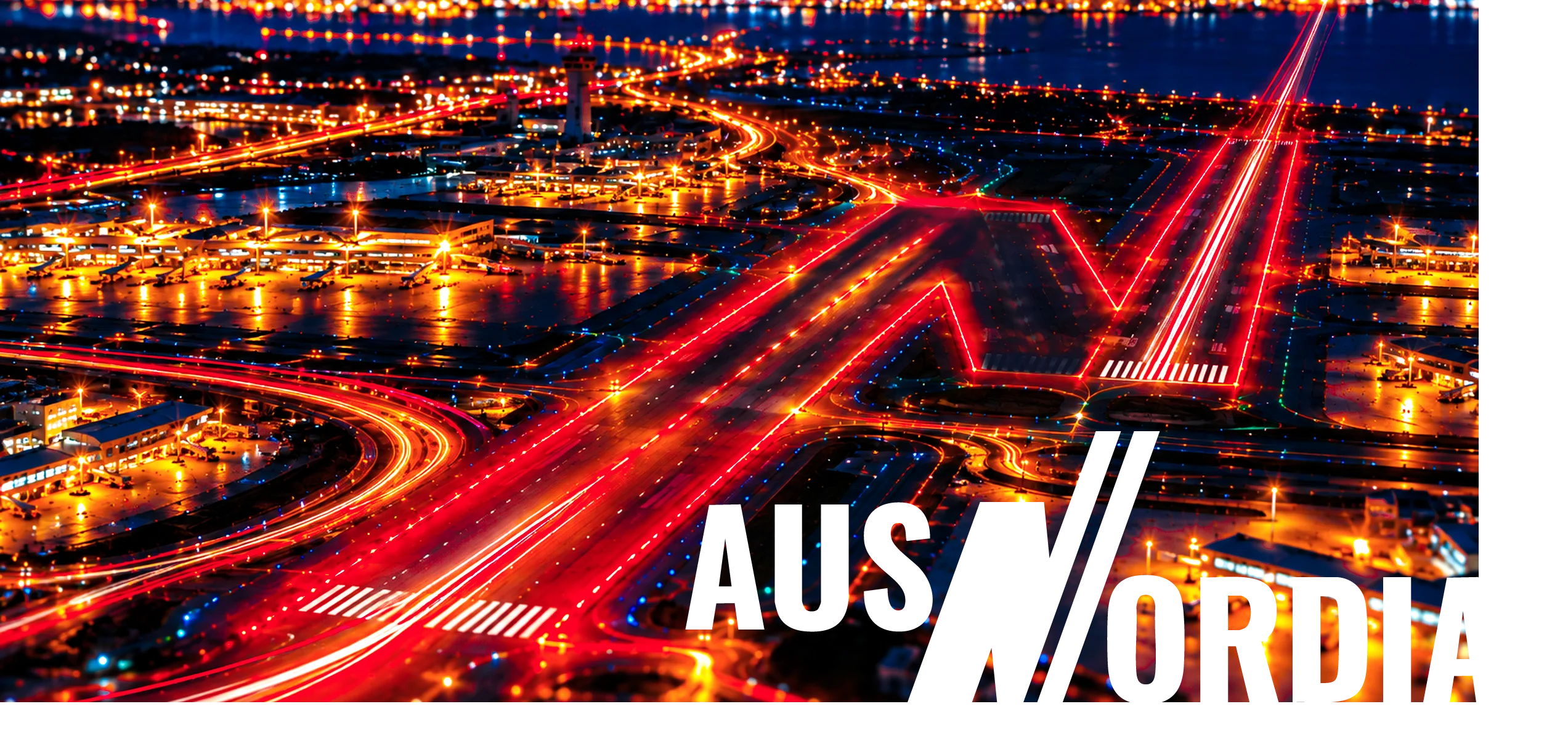 An illuminated N-shaped runway at night, with a take-off light streak rising towards the horizon.